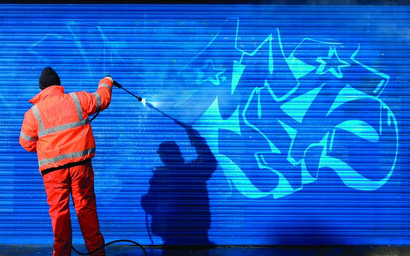 A worker cleaning graffiti from a shutter